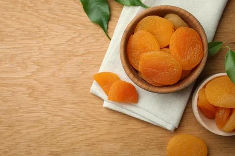 Tasty apricots with bowl on wooden table, flat lay and space for text. Drie.. Stock Photos