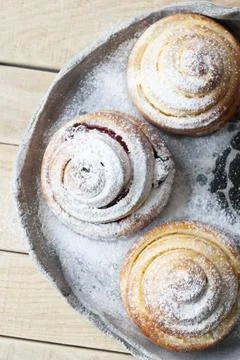 Tasty buns are sprinkled with sugar powder on a light hand-made plate on a .. Stock Photos