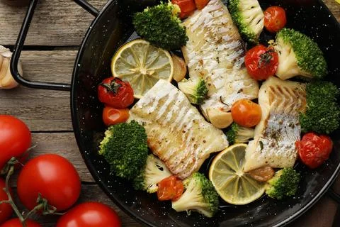 Tasty cod cooked with vegetables in frying pan on wooden table, flat lay Stock Photos