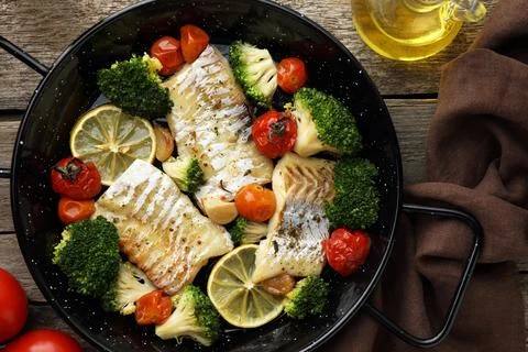 Tasty cod cooked with vegetables in frying pan on wooden table, flat lay Stock Photos