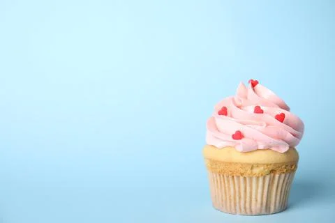 Tasty cupcake with heart shaped sprinkles on light blue background, space for Stock Photos