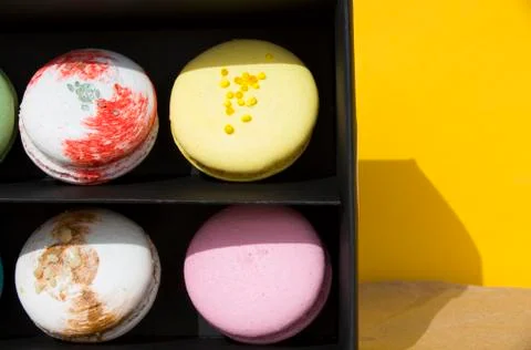 Tasty different colored macarons in black box on yellow background 库存照片