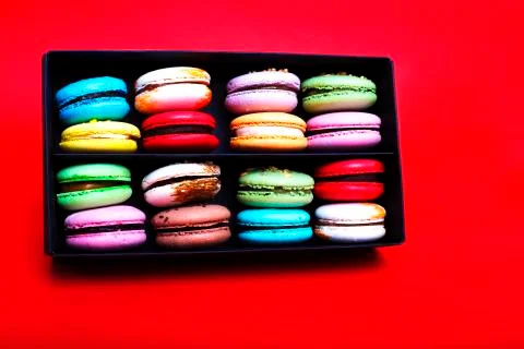 Tasty different colored macarons in black box on red background. Stock Photos