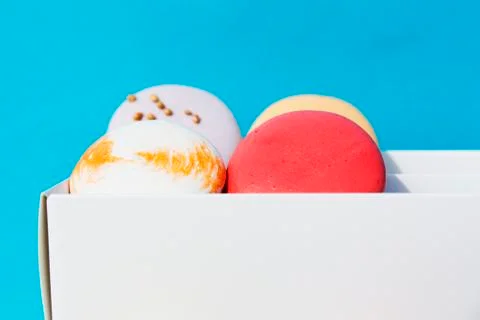 Tasty different colored macarons in white box on blue background 库存照片