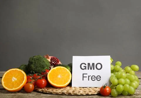 Tasty fresh GMO free products and paper card on wooden table against grey bac Stock Photos