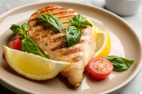 Tasty grilled chicken fillet with green basil, lemon slices and tomato on pla Stock Photos