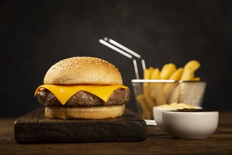 Tasty hamburger with french fries and sauces on dark background. Stock Photos