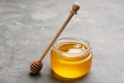 Tasty honey and wooden dipper on light grey table Stock Photos