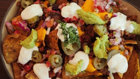 Tasty nachos topped with smashed beef, melted cheese, jalapenos, tomatoes Stock Footage 320558912