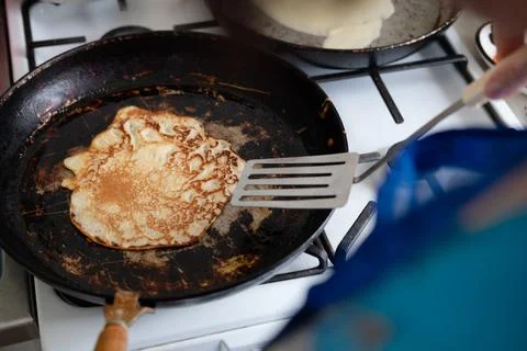 Tasty pancake in a cast-iron pan. Fry a delicious pancake in a rustic cast ir Stock Photos