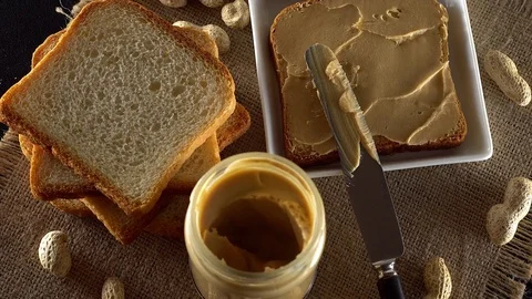 Tasty peanut butter being spread on white toast Видео 71370499
