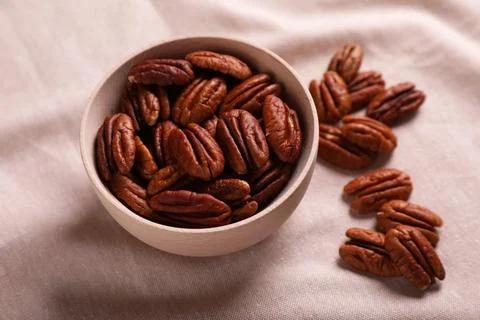 Tasty pecan nuts with bowl on beige cloth, closeup Stock Photos