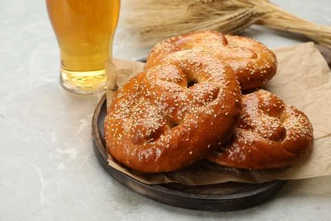 Tasty pretzels, glass of beer and wheat spikes on light grey table Stock Photos