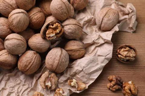 Tasty walnuts and parchment paper on wooden table, closeup Stock Photos