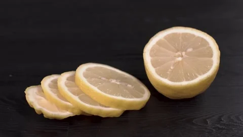 Tasty yellow sliced lemon rotating on black wooden table close up view. Stock Footage 149003297