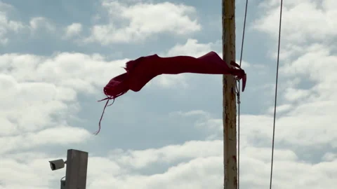 Tattered Red Flag Blusters on Rusty Pole Against a Cloudy Sky Stock Footage 333562488