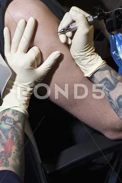 A tattoo artist preparing to tattoo a man's bare arm, close-up Stock Photos