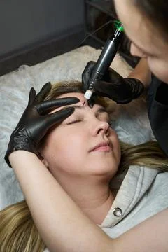 Tattoo master doing permanent makeup to a woman Stock Photos
