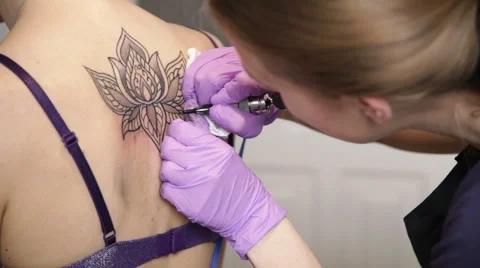 Tattoo master is making tattoo flower on the woman's back, close up Stock Footage 63088761