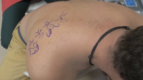 Tattoo master is preparing to make a tattoo "little men" on the back of a man Stock Footage 118200925