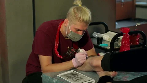 Tattoo master with tattoo machine makes a tattoo for a girl in tattoo parlor. Stock Footage 118635850