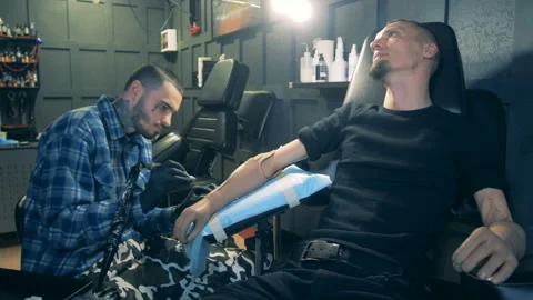 Tattoo salon with a disabled man getting a tattoo on his prosthesis Stock Footage 103271222