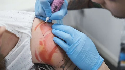 Tattoo Studio, guy gets color tattoo on his arm, it's bleeding Stock Footage 127551471