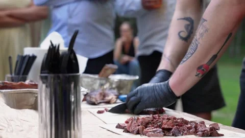 Tattooed Chef Slicing Grilled Meat Outdoors at Casual Gathering Stock Footage 339201558