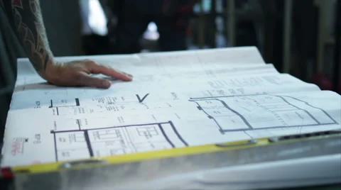 Tattooed Construction Worker Clears Dust from Workbench and Reviews Blueprints Stock Footage 40646400