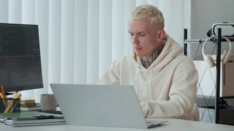 Tattooed Developer Analyzing Coding Screens on Laptop and Computer Monitor Stock Footage 303557369