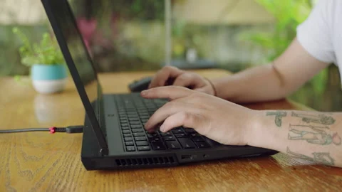 Tattooed developer types code on laptop, programing in a cozy cafe. Focused on Stock Footage 264477083