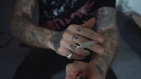 Tattooed hand rolling a marijuana joint smoke Stock Footage 90021925