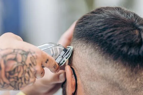 Tattooed hand using a shaving machine to cut hair of a costumer in a barber shop Stock Photos