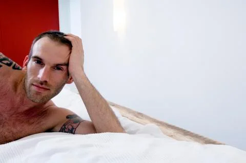 Tattooed man, barechested, lying in bed, looking at the camera Stock Photos