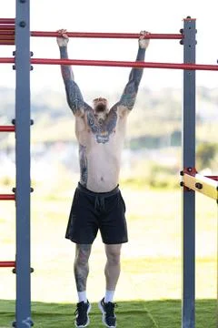 Tattooed man hanging from pull up bar Stock Photos