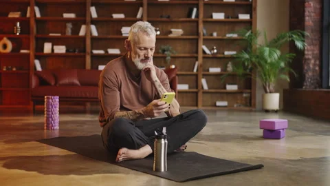 Tattooed man in his 50s browsing a fitness app and choosing a yoga exercise Stock Footage 340902178