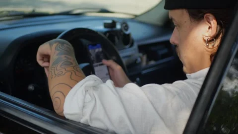 Tattooed man sitting in car using smartphone, scrolling... Vidéo 324632408