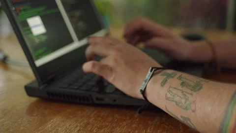 Tattooed programmer types code on laptop, debugging software project. Pro Stock Footage 270534897