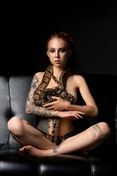 Tattooed woman on the sofa with python shot Stock Photos