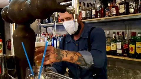 Tattooed young man in mask serving beer during the coronavirus Covid-19 Stock Footage 132328209