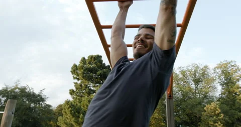 A tattooed young man smiling while using the bars at the outdoor gym. Stockbeeldmateriaal 130219629
