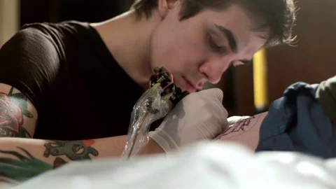 Tattooist does tattoo to a client in a tattoo parlor Video stock 76933112