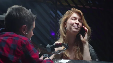 Tattooist makes a tattoo while a client is talking on the phone Stock Footage 131064918