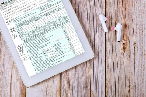Tax 1040 form document displayed on tablet with wireless earbuds on account.. Stock Photos