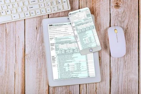 Tax forms displayed on PC tablet smartphone next to computer keyboard mouse.. Stock Photos