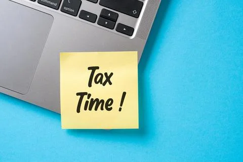 Tax Time written on a sticky note stuck to the corner of a laptop on a blue.. Stock Photos