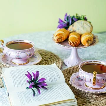Tea and snacks set on a table with flowers and a book Fotos de archivo