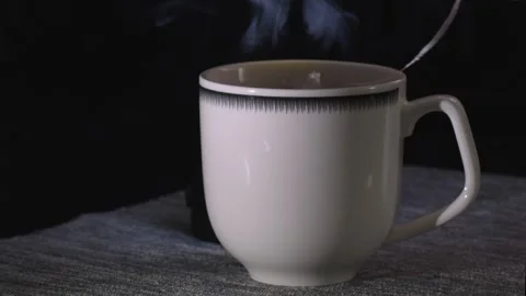 Tea bag being dipped into white cup with boiling water, dark background, stea Stock Footage 306357426