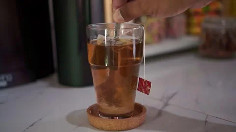 Tea bag brewing in glass filled with hot water and spoon stirring, Stock Footage 342634867