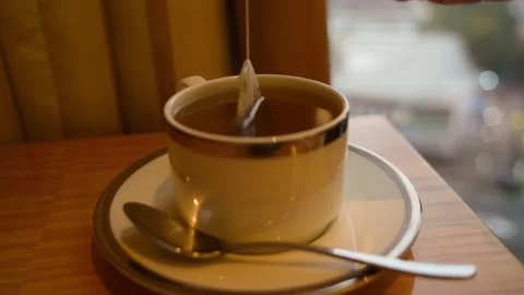 Tea Bag Dipping and Steeping in Cup of Hot Tea on Hotel Table by Window 스톡 동영상 330392529